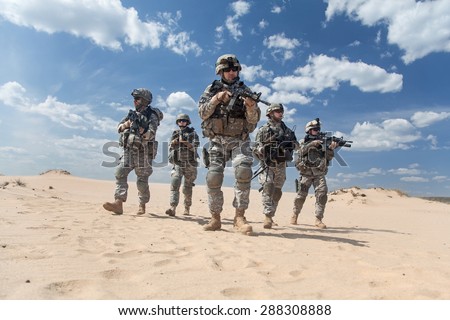 Team of United states airborne infantry men with weapons moving patrolling desert. Sand and blue sky on background of squad, sunlight, front view