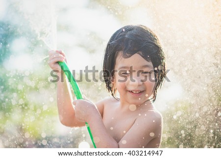 Cute asian boy has fun playing in water from a hose outdoors