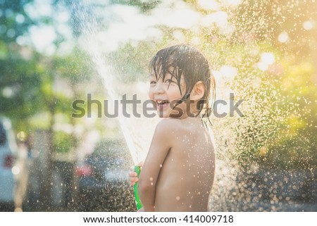 Cute asian boy has fun playing in water from a hose outdoors