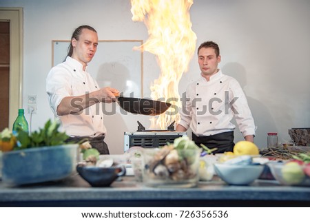 Two Chefs Flaming The Dishes In Their Kitchen Frying Some Exotic Food