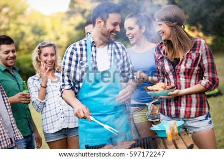 Happy friends grilling meat and enjoying barbecue party outdoors