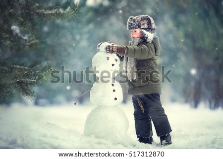 Cute little boy in earflaps hat is making a snowman. Image with selective focus and toning
