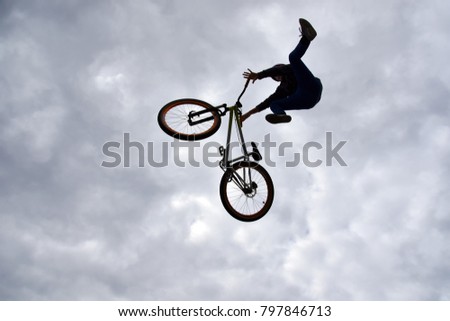 Sofia, Bulgaria - September 23, 2017: Back lit dark silhouette of a young boy - freestyle stunt cyclist - flying in the sky with his bike, performing a trick - jump from a skate-park ramp