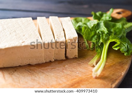 Slices of uncooked tofu and green leaves of fresh spinach on cutting board