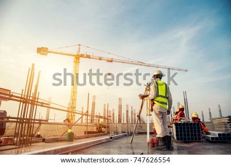 Surveyor builder Engineer with theodolite transit equipment at construction site outdoors during surveying work