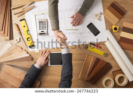 Architect and customer businessman shaking hands top view, desktop with building project, tools and wood swatches on background