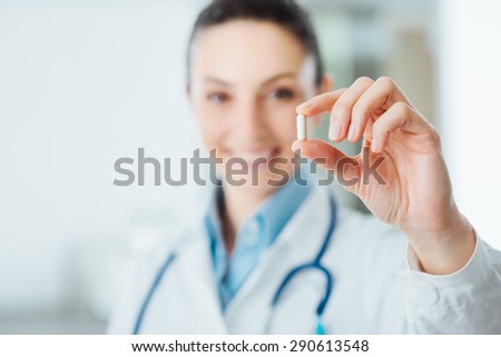Smiling female pharmacist holding a pill, health care and prevention concept, hand close up