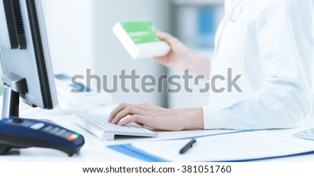 Pharmacist holding a medicine packet and searching that product in the computer database, healthcare and technology concept