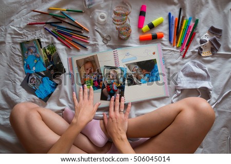 Photos in hands and photo album on grey blanket in the bed, Creating photo book for child with Down's syndrome