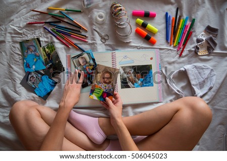Photos in hands and photo album on grey blanket in the bed, Creating photo book for child with Down's syndrome