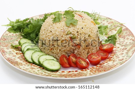 A healthy tomato (thakkali) biriyani with a salad of cucumber, cherry tomatoes and some fresh leaves. This biryani, which incorporates onion, peas and a capsicum ball pepper, is a South Indian dish. - stock photo