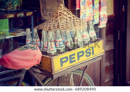 Bangkok, Thailand - May 7, 2017: Vintage retro style of Pepsi bottles stacked in grunge wooden container on retro bike with retro shop background in Traditional Baan Bangkhen Museum in Bangkok.