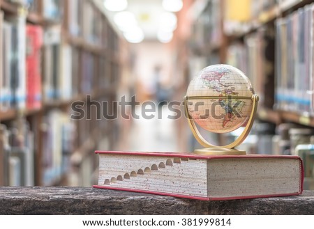 FEBRUARY 26, 2016 - BANGKOK, THAILAND: Globe model on textbook, book on old age wood table, blur abstract campus school library background, stack of special knowledge resource, educational data aisle