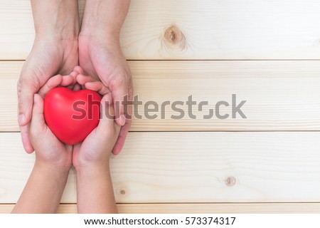 Mom Mother's hand holding daughter, son child kid palm supporting red heart love ball on light white wood background: Nursing children home day care health care concept: Hospital medical business