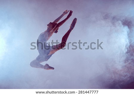 young ballet dancer jumping on a lilac background. Ballerina is wearing in blue dress and pointe shoes. The outline shooting - silhouette of girl with smoke effect