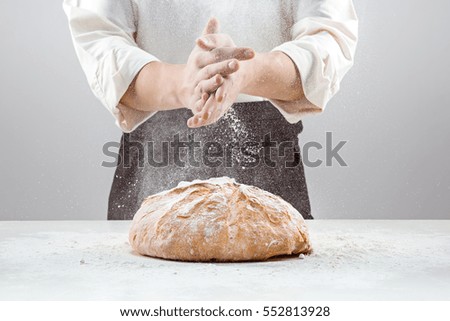 The male hands in flour and rustic organic loaf of bread