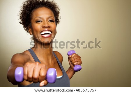 Happy African American fitness woman lifting dumbbells smiling and energetic.
