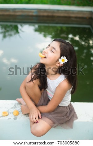 stock photo little preteen brunette girl with long dark hair and flower in hair sitting barefoot by the pool in 703005880