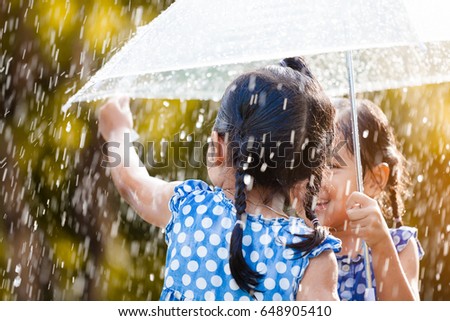 Back view of two happy asian little girls with umbrella having fun to play with the rain together in vintage color tone