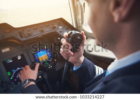 Close up pilot hand taking by portable radio set in cabin while navigating plane. Occupation and communication concept