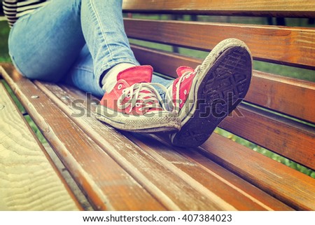 stock-photo-woman-s-legs-in-a-blue-jeans-and-red-canvas-sneakers-sitting-on-a-bench-retro-styled-photo-407384023.jpg