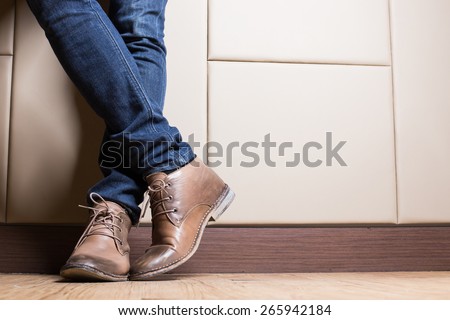 Young fashion man's legs in blue jeans and brown boots on wooden floor