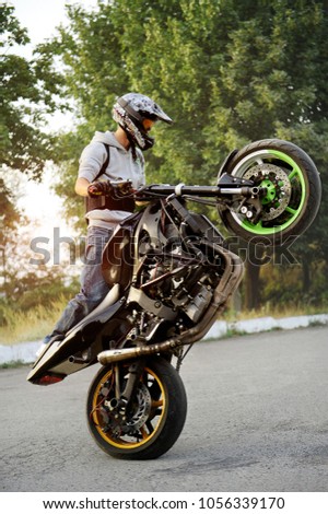 Ivano-Frankivsk, Ukraine - 28 August 2015 : Good photo of a stuntman doing trick riding motorcycle on one cycle along the street. Green tricks on background. Summer sunset.