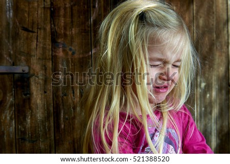 Little child sad crying girl on the background of an old wooden wall