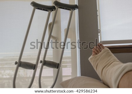 Người khuyết tật bị thương Với Ankle vỡ bong gân vàng chân vàng Với Nạng Ngồi Bên Nhìn bên ngoài cửa sổ trượt cửa kính là Sunny Day.