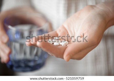 Cuidados de saúde, tratamento, foto do conceito de suplementos.  Braço de mulher segurando um monte de pequenos remédios redondos e copo de água antes de tomar medicação, profundidade de campo rasa, foco em medicina