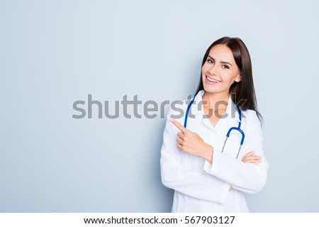 Friendly smiling young female doctor pointing with finger.