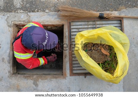 Muadzam Shah, Malaysia - March 22nd, 2018: Municipal worker "Alam Flora" uses sweepers and shovels to clean the garbage in the drain and put into the garbage bag.