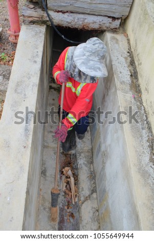 Muadzam Shah, Malaysia - March 22nd, 2018: Municipal worker "Alam Flora" uses sweepers and shovels to clean the garbage in the drain and put into the garbage bag.