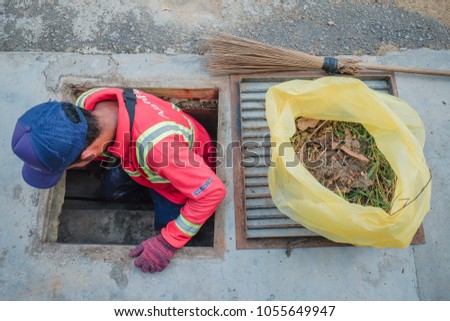 Muadzam Shah, Malaysia - March 22nd, 2018: Municipal worker "Alam Flora" uses sweepers and shovels to clean the garbage in the drain and put into the garbage bag.