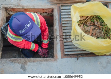 Muadzam Shah, Malaysia - March 22nd, 2018: Municipal worker "Alam Flora" uses sweepers and shovels to clean the garbage in the drain and put into the garbage bag.