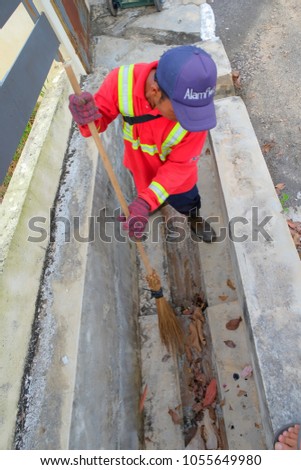 Muadzam Shah, Malaysia - March 22nd, 2018: Municipal worker "Alam Flora" uses sweepers and shovels to clean the garbage in the drain and put into the garbage bag.