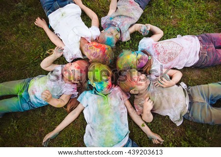 Children lie on the grass. Children painted in the colors of Holi festival lie on the grass.