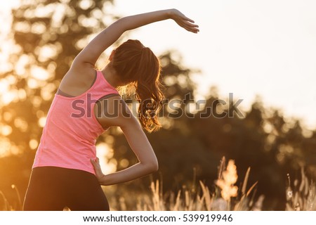 Young female  stretching before fitness training session at the park. Healthy young woman warming up outdoors. She is stretching her arms and looking away,hi key.