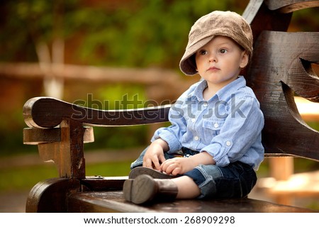 little boy in the blue shirt and brown cap is sitting on the wooden bench in - Pictures For Little Boys little boy in the blue shirt and brown cap is sitting on the wooden bench in - Pictures For Little Boys
