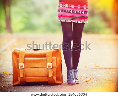 Women's foots near suitcase at autumn outdoor.