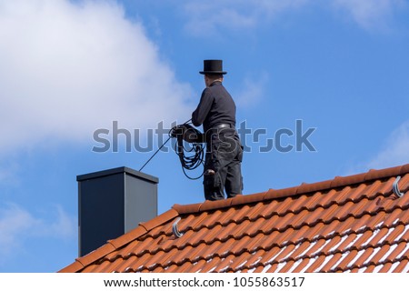 Chimney sweep cleaning a chimney standing on the house roof, lowering equipment down the flue