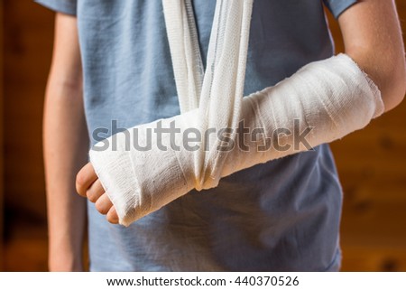 Child stands with broken arm in gypsum on the brown background; being in hospital, injury and health concept