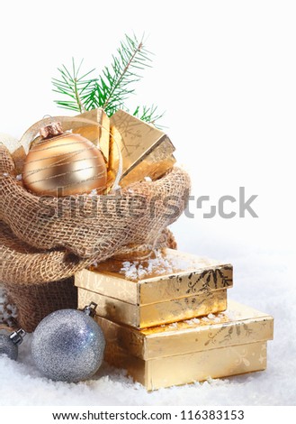 Rustic Christmas gift background with decorative baubles and golden gifts spilling out of a simple hessian sack onto the snowcovered ground with copyspace