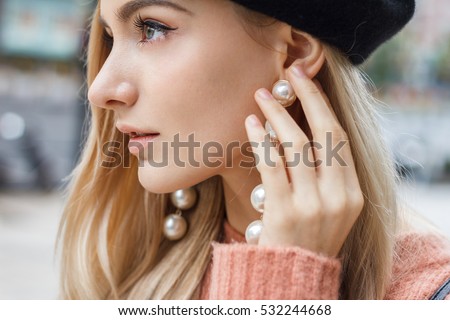 Close up detail of beautiful young blonde woman dressed in pink sweater with gorgeous earrings made of big pearls.