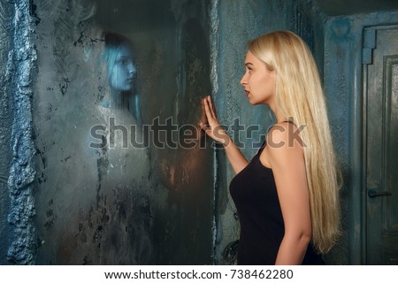 Frightened young woman looking to the mirror and seeing in reflection a ghost girl Frightened young woman looking to the mirror and seeing in reflection a ghost girl