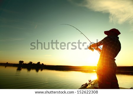 Young man fishing on a lake from the boat at sunset