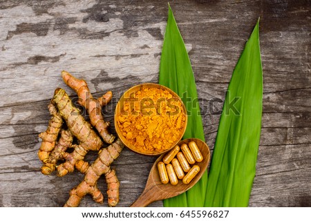 Turmeric powder in wooden bowls and turmeric capsules on wooden background