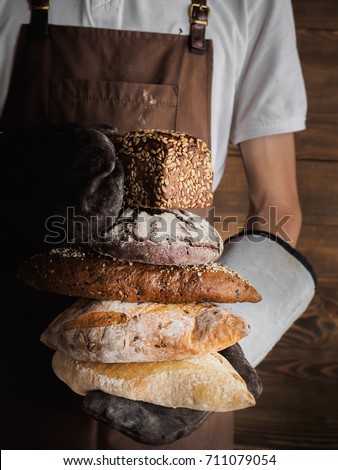 Variety of freshly baked breads in a young bakers hands. Hipster nordic baker with rye, wholewheat and white bread close up.