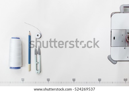 Tailor supplies frame, free space on white background. Top view on sewing machine platform with thread, scissors and pencil on it. Cope space for text. Garment industry backdrop