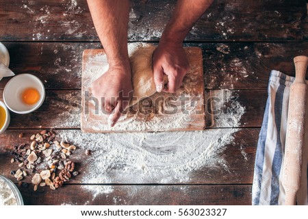 Hands kneading raw dough on table flat lay. Top view on baker workplace, working with pastry, free space on flowered table. Culinary, cooking, bakery concept